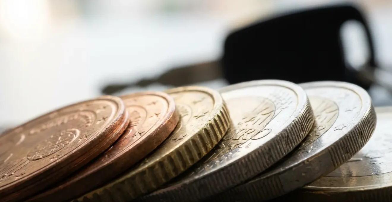 Vue macro sur des pièces d'euros empilées avec reflet d'une clé de voiture floue en arrière-plan