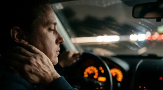 Conducteur fatigué se massant la nuque au volant de nuit sur l'autoroute