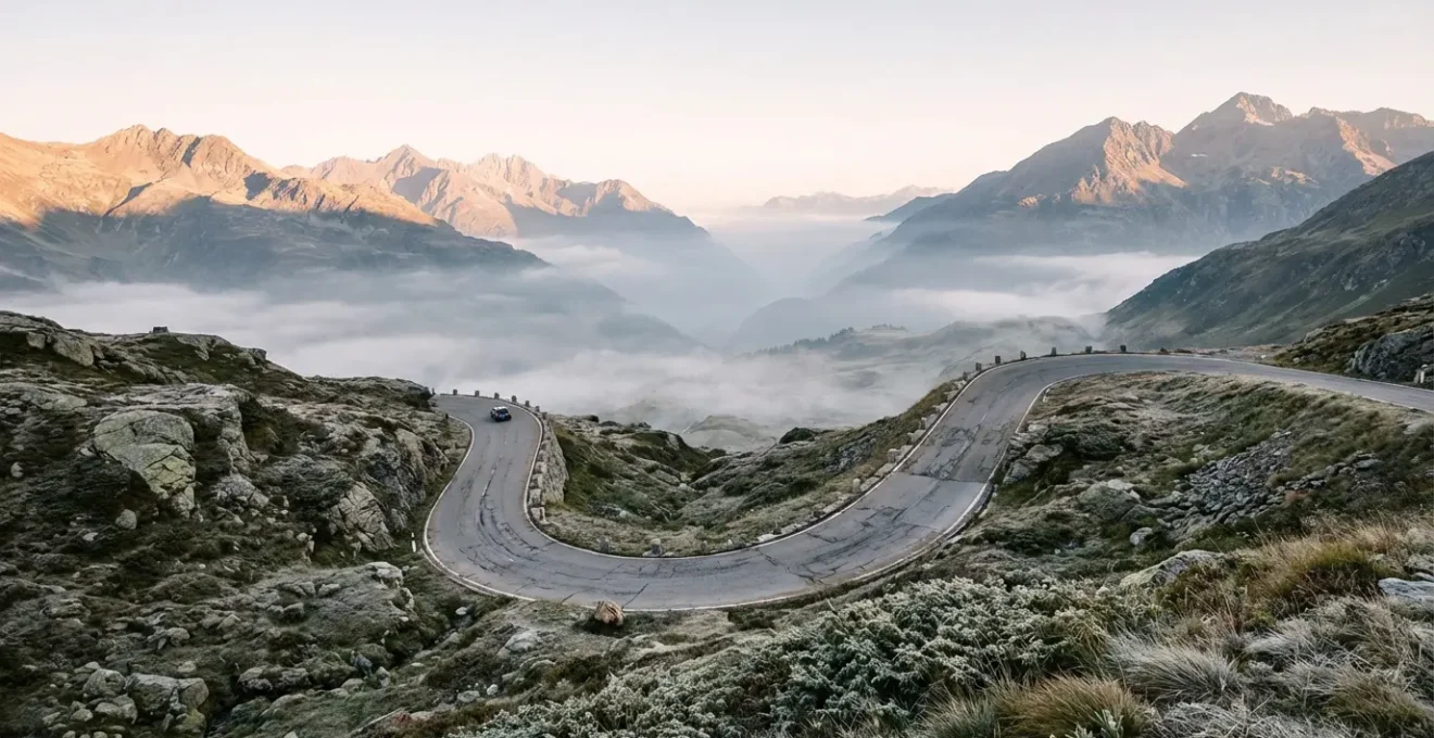 Vue grand angle d'une route de montagne sinueuse avec véhicule isolé dans un paysage alpin