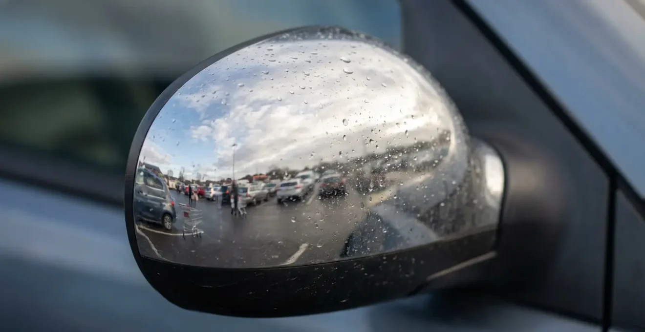 Vue macro détaillée d'un rétroviseur de voiture reflétant un parking avec véhicules et piétons