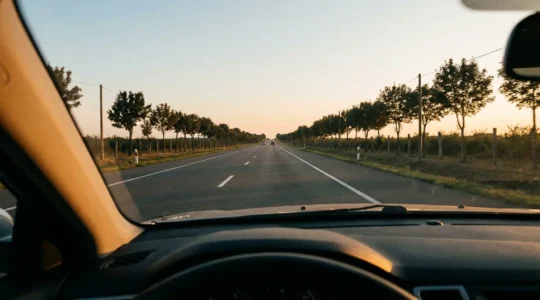 Vue depuis l'habitacle d'une voiture montrant une route dégagée s'étendant au loin avec des éléments de signalisation